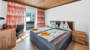 A bedroom with a wooden ceiling, a bed with pillows, a desk, and a chair.