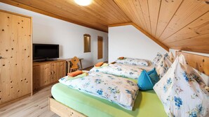 A bedroom with a wooden ceiling, a television, two beds with floral bedding, and a wooden wardrobe.