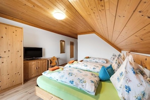 Un dormitorio con techo de madera, televisor, dos camas con ropa de cama floral y un armario de madera.