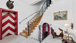 Eine Treppe mit einer Tür im Zickzackmuster, einem aufgehängten Tierkopf, einem Gemälde und einer Lampe.