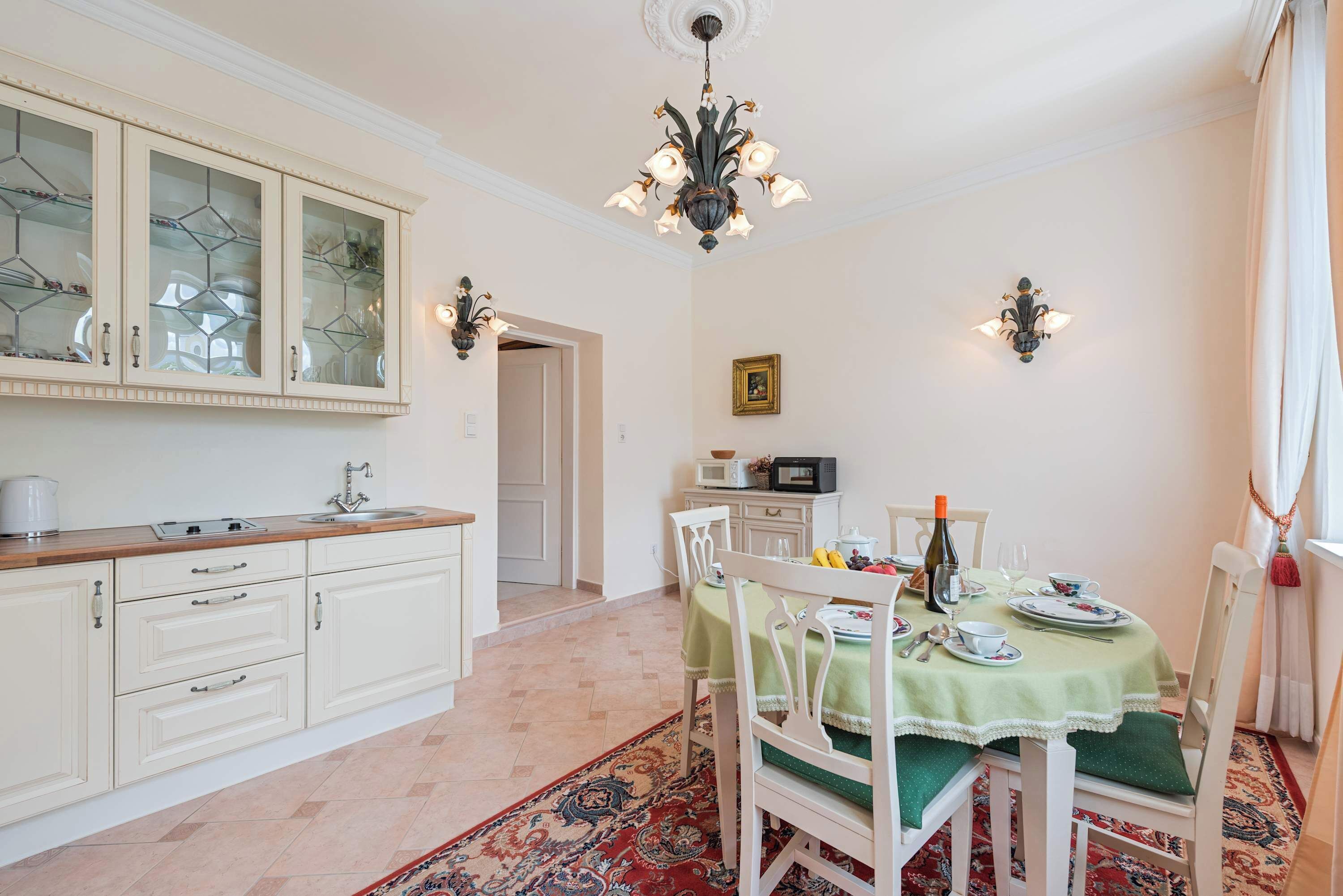 Een eetgedeelte met een tafel voor vier personen, een keuken met witte kastjes en een kroonluchter.