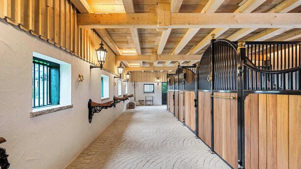 A corridor with wooden beams, a brick floor, and a stable area with black gates.