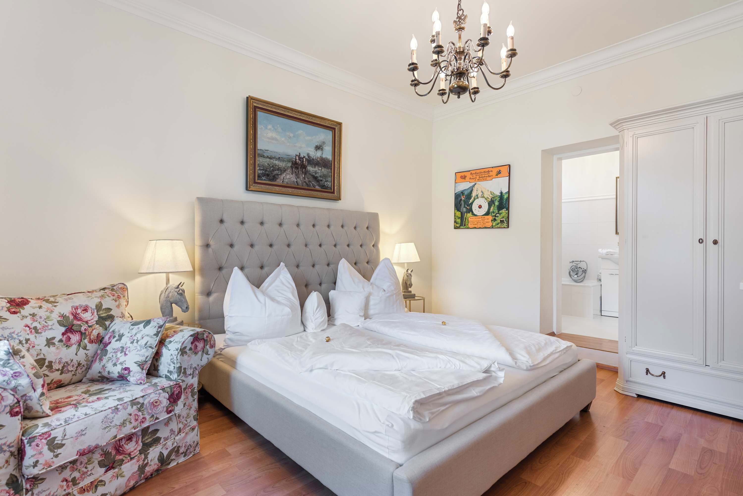 Una camera da letto con un letto, un divano floreale, un lampadario, un quadro incorniciato e un armadio.