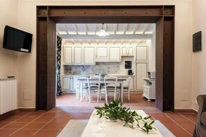 A kitchen with white cabinets, a dining table with chairs, a TV mounted on the wall, and a hanging light fixture. - Stone farmhouse in the Chianti hills (Montaione)