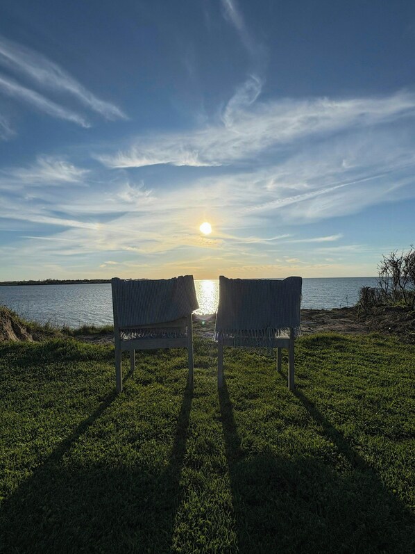 Two chairs facing a body of water with the sun low on the horizon.