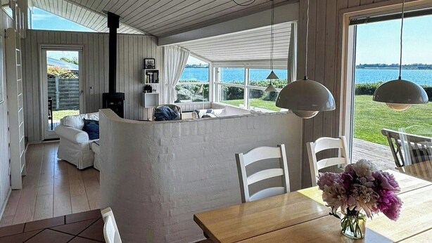 Ett rymligt vardagsrum med ett stort fönster, ett träpanelat tak och ett matbord med stolar.