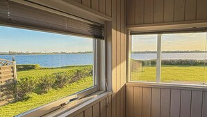 Ett rum med träpanel på väggarna, utsikt över en sjö eller ett annat vattendrag och ett fönster med utsikt över en gräsyta.