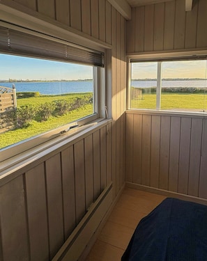 Ein Zimmer mit Holzwänden, Blick auf ein Gewässer und ein Fenster mit Blick auf eine Wiese.