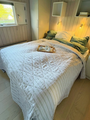 Ein Schlafzimmer mit einem Bett, einem Tablett mit Tassen und einer Karaffe, einem Fenster und einer Tür.
