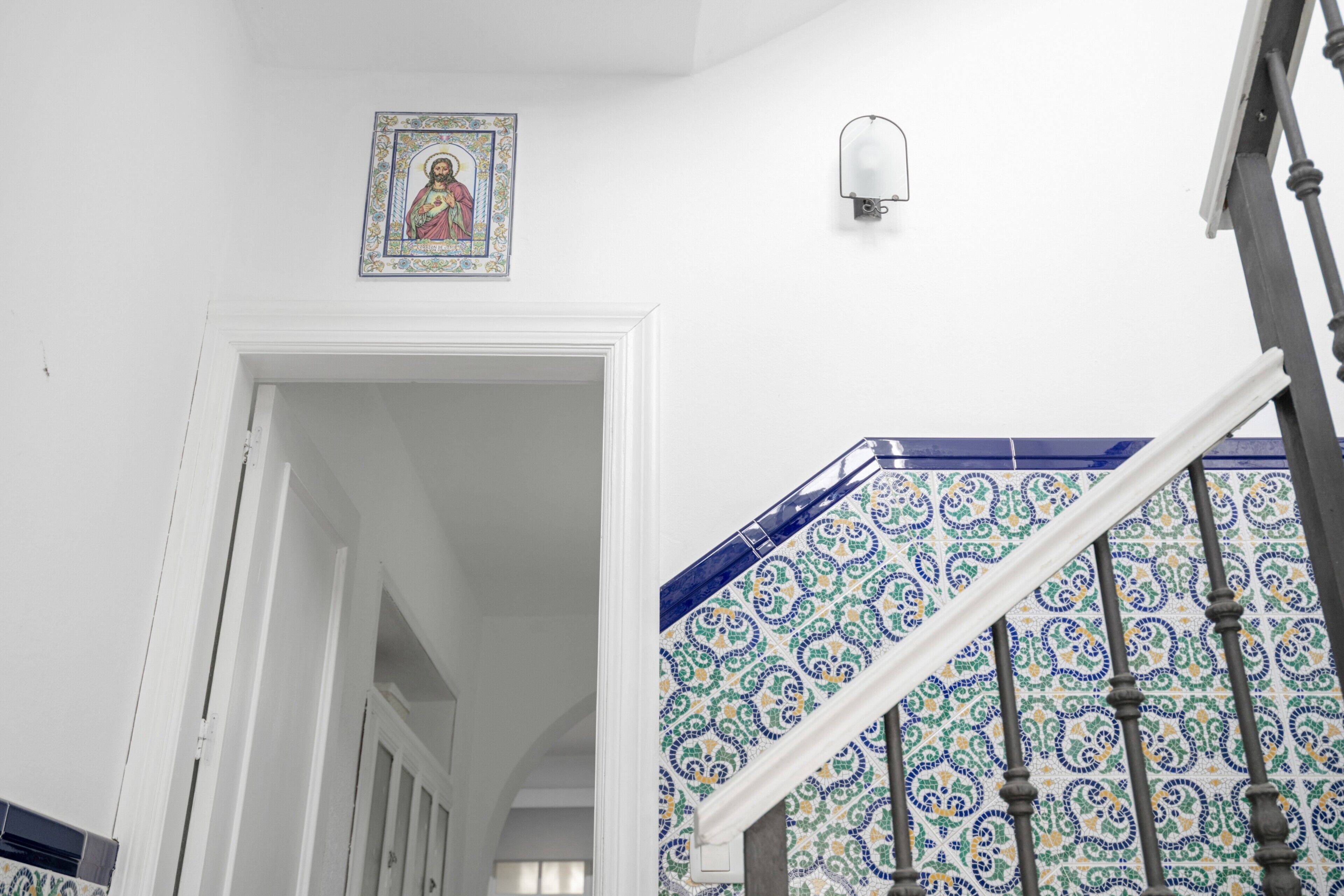 A staircase with ornate blue and white tiles, a white door frame, and a wall-mounted light fixture.