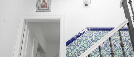 A staircase with ornate blue and white tiles, a white door frame, and a wall-mounted light fixture.