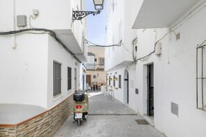 A narrow alleyway with a scooter parked on the left, white buildings with visible windows and doors, and overhead electrical wires. - Holiday Home 'Playa De Conil' with Wi-Fi (Conil de la Frontera)