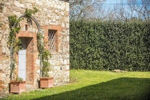 Ein Steinhaus mit Fenster und Tür, umgeben von einer gepflegten Hecke und einer Rasenfläche.