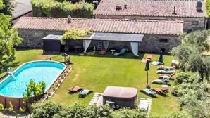 A pool with a grassy area, lounge chairs, and a stone building with a tiled roof. - Panoramic guesthouse in the Siena hills (Castelnuovo Berardenga)