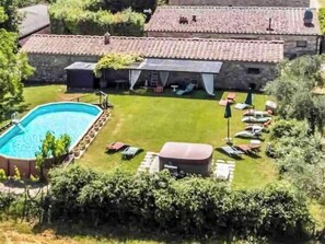 Ein Pool mit Rasenfläche, Liegestühlen und einem Gebäude mit steinernen Wänden und einem Ziegeldach.