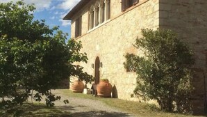 A stone building with a central arched doorway, flanked by two large terracotta pots, and surrounded by greenery. - Panoramic guesthouse in the Siena hills (Castelnuovo Berardenga)