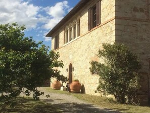 Ein Steinhaus mit einem zentralen Bogenportal, das von zwei großen Terrakottatöpfen flankiert wird, umgeben von Grünpflanzen.