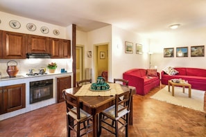 A kitchen with wooden cabinets, a dining table with chairs, a red sofa, and a small table with a lamp.