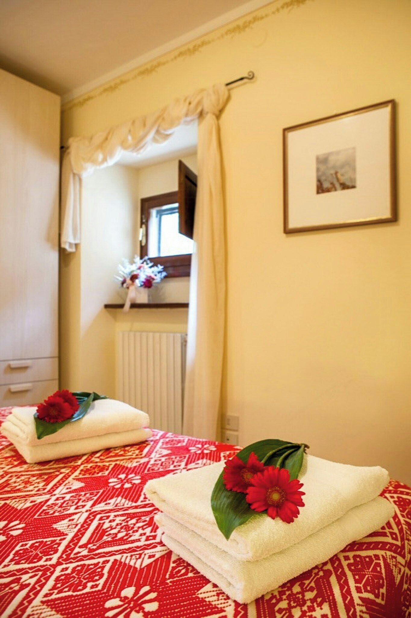 Een hotelkamer met een bed, een raam met gordijnen, een ingelijst schilderij aan de muur en een radiator.