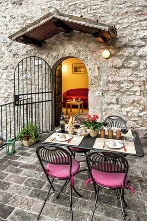 An outdoor dining area with stone walls, a wrought iron gate, and a red interior visible through an archway. - Medieval tower with terrace in Rasiglia (Rasiglia)