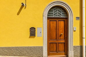 A yellow building with a double wooden door, a mailbox, and a number plate.