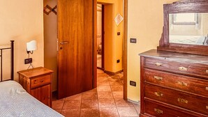 Une chambre à coucher comprenant un lit, une commode en bois, une table de chevet et une porte donnant sur une autre pièce.