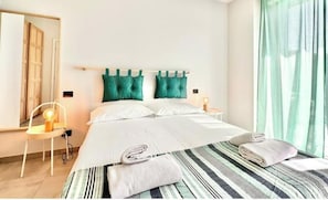 Et hotelværelse med en seng, en stol, en lampe og et vindue med gardiner.