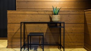 Een zwarte metalen tafel met een rieten mand waarin een plant staat, tegen een houten muur geplaatst.