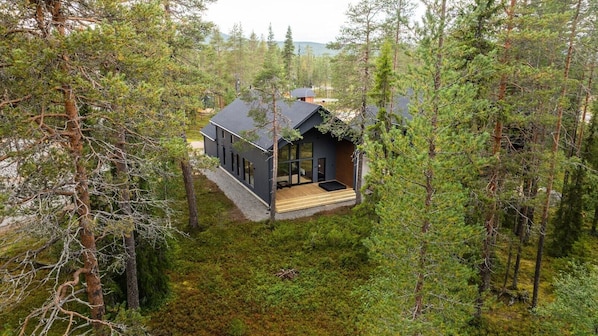 A cabin surrounded by dense forest, with a wooden deck and large windows.
