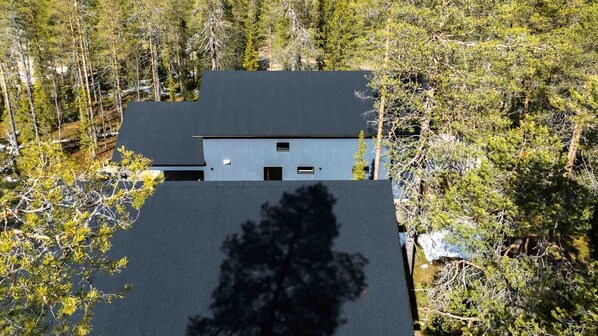 Un edificio moderno de dos pisos con techo plano, rodeado de un bosque denso.