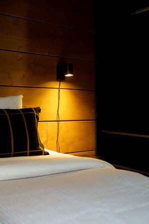 A bed with white bedding and a black headboard, a black wall-mounted lamp, and a wooden panel wall.