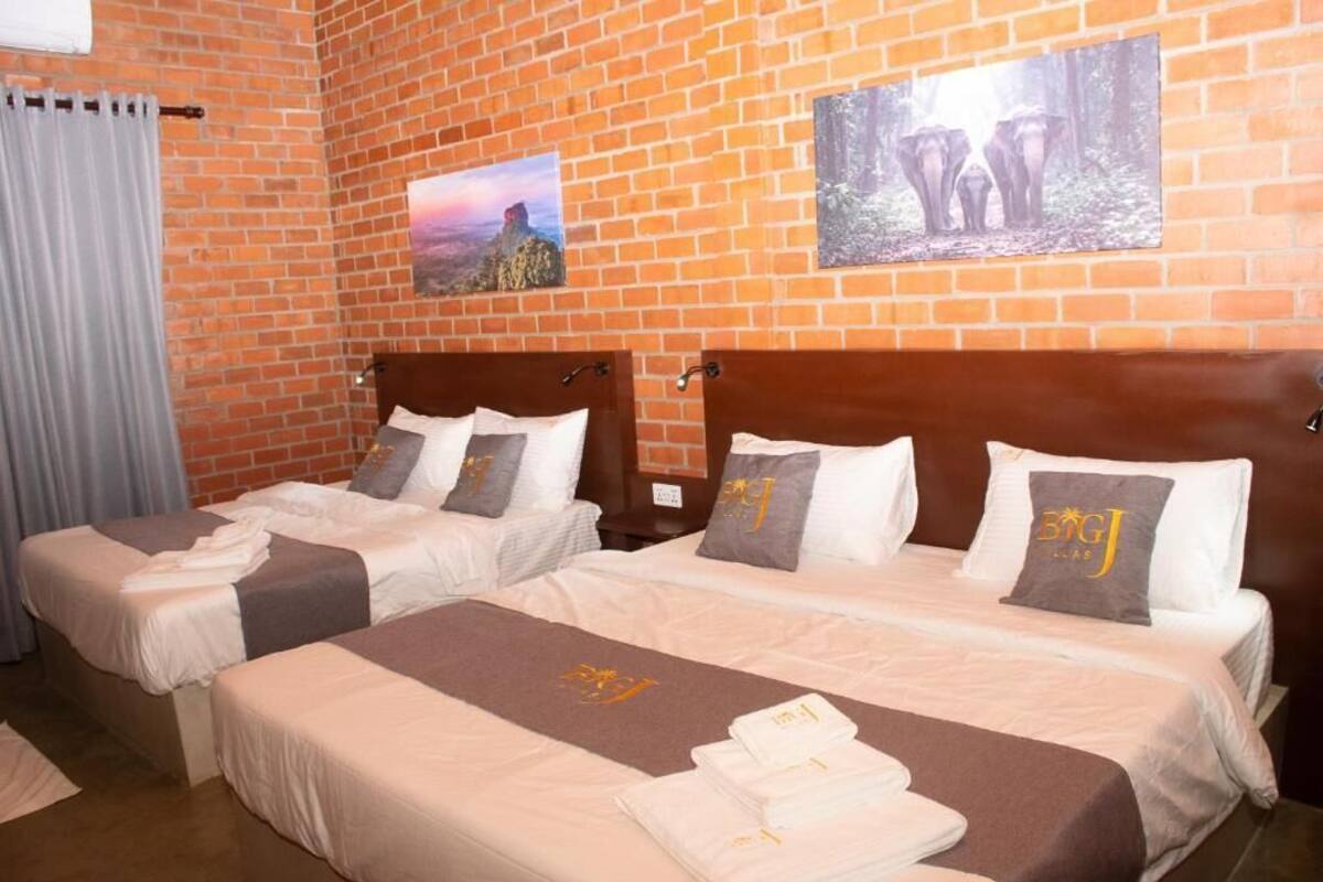 A hotel room with two beds, a brick wall, and two framed pictures.