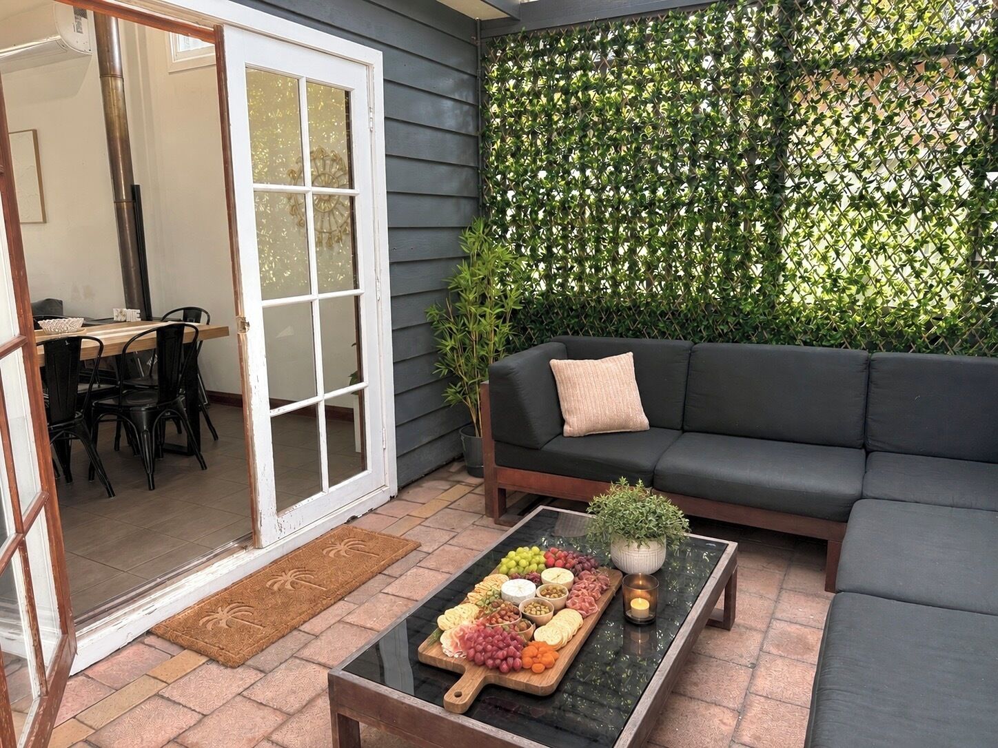 Une terrasse avec une table en verre, un canapé noir et une plante verte.
