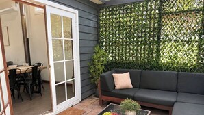 Een terras met een glazen tafel, een zwarte bank en een groene plant.