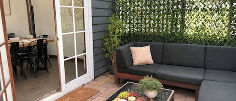 A patio with a glass table, black sofa, and a green plant.