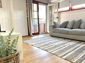 A living room with a sofa, a patterned rug, a wooden floor, and a sliding glass door leading outside. - Mahalo at Anna Bay (Anna Bay)