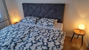 Ein Bett mit gemustertem Überwurf, einem gepolsterten Kopfteil und zwei Nachttischlampen.