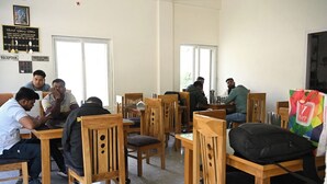 A room with wooden chairs and tables, a reception desk, and a sign indicating a check-out time. - Hotel Uday Villa (Rajgarhi)