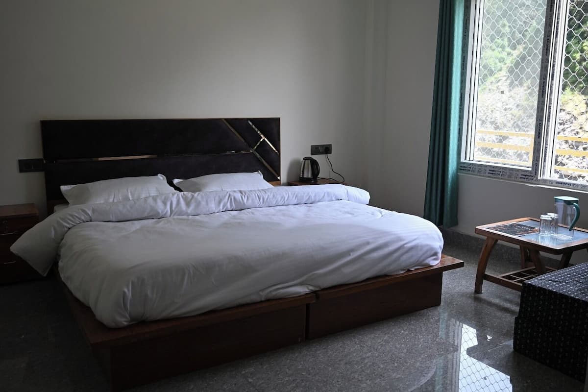 Una cama bien hecha con sábanas blancas, un cabecero de madera, una mesita de noche con lámpara y una ventana con vista a la vegetación.