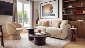 Una sala de estar moderna con un sofá, una mesa redonda de centro, una silla, una estantería y una obra de arte grande enmarcada.