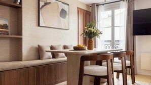 Una sala de estar moderna con un sofá, una mesa de comedor con sillas, un televisor y una ventana con cortinas.
