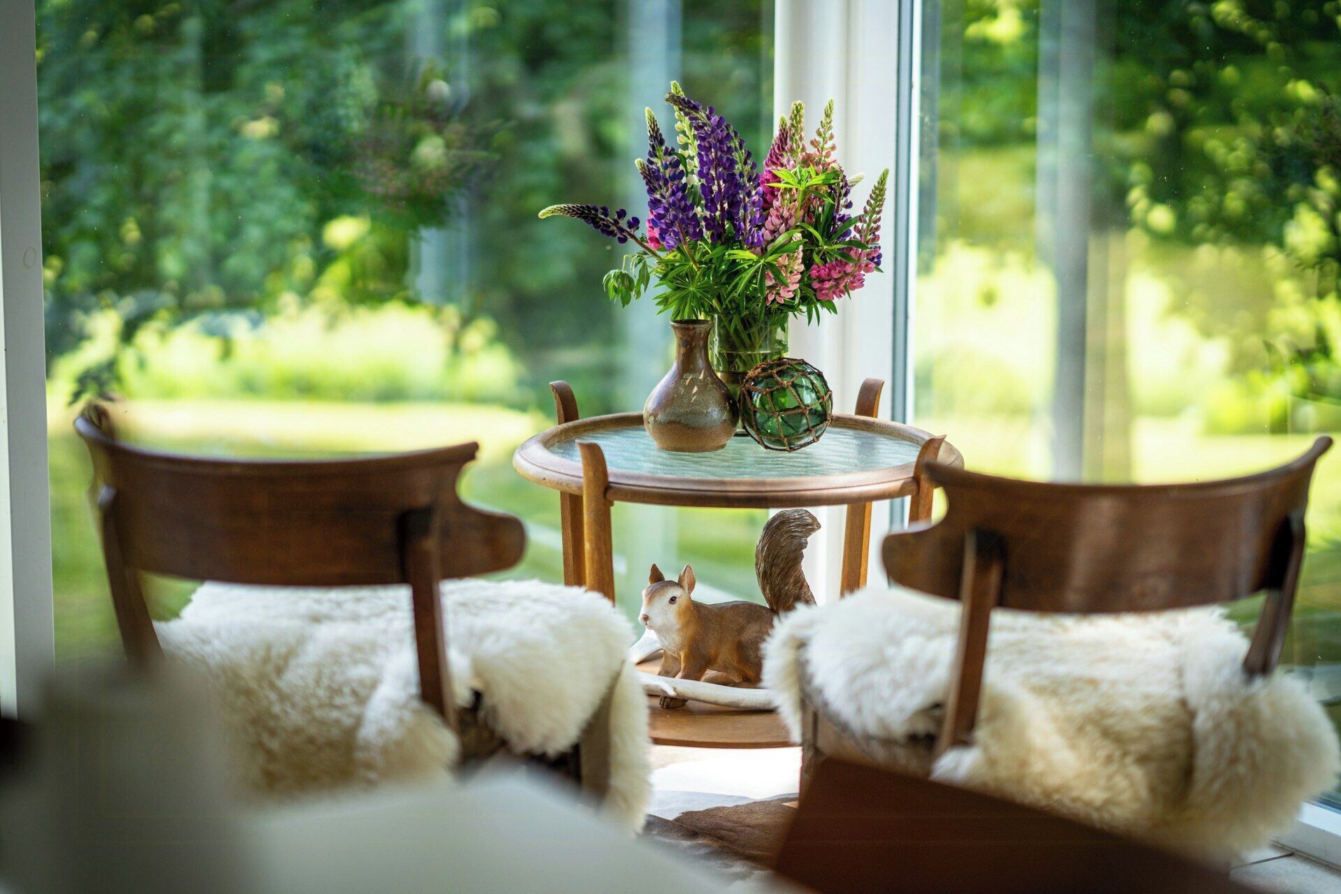 A table with a vase of flowers, two chairs, and a small animal figurine.