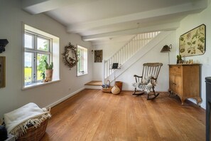 Una habitación amplia con piso de madera, una escalera, un sillón mecedor y un armario.