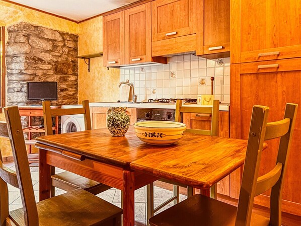 Una cocina con armarios de madera, pared de piedra, salpicadero de azulejos y una mesa de comedor de madera con sillas.