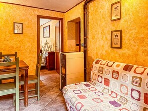 Una habitación con cama, una mesa, sillas, una pequeña cocina y una puerta que da a otra habitación.