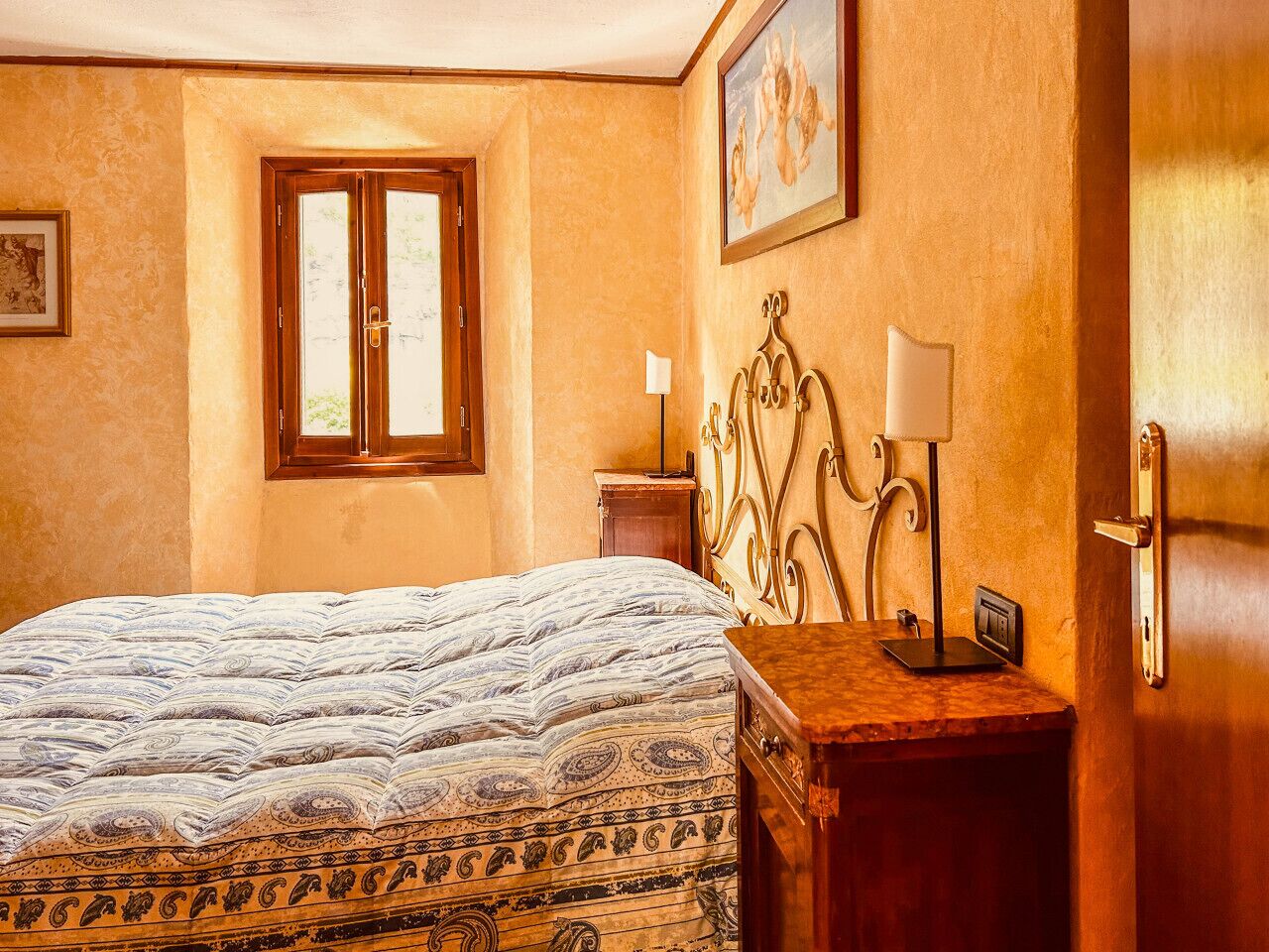 A bedroom with a bed, a nightstand, a lamp, a painting, and a window.