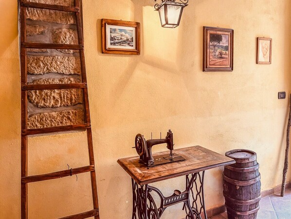 A vintage sewing machine on a wooden table, a wooden ladder, and a barrel against a textured wall with framed pictures.