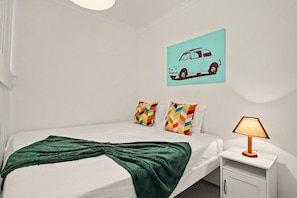 A neatly made bed with a green blanket, a bedside lamp, and a wall-mounted car illustration. - Sun & Green Apartment – Near Tavira and the Beach (Conceição)