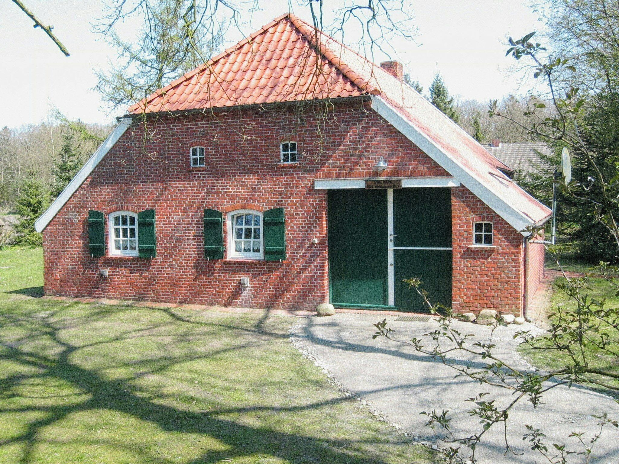 A small brick house with a red roof, two windows with green shutters, and a green door.