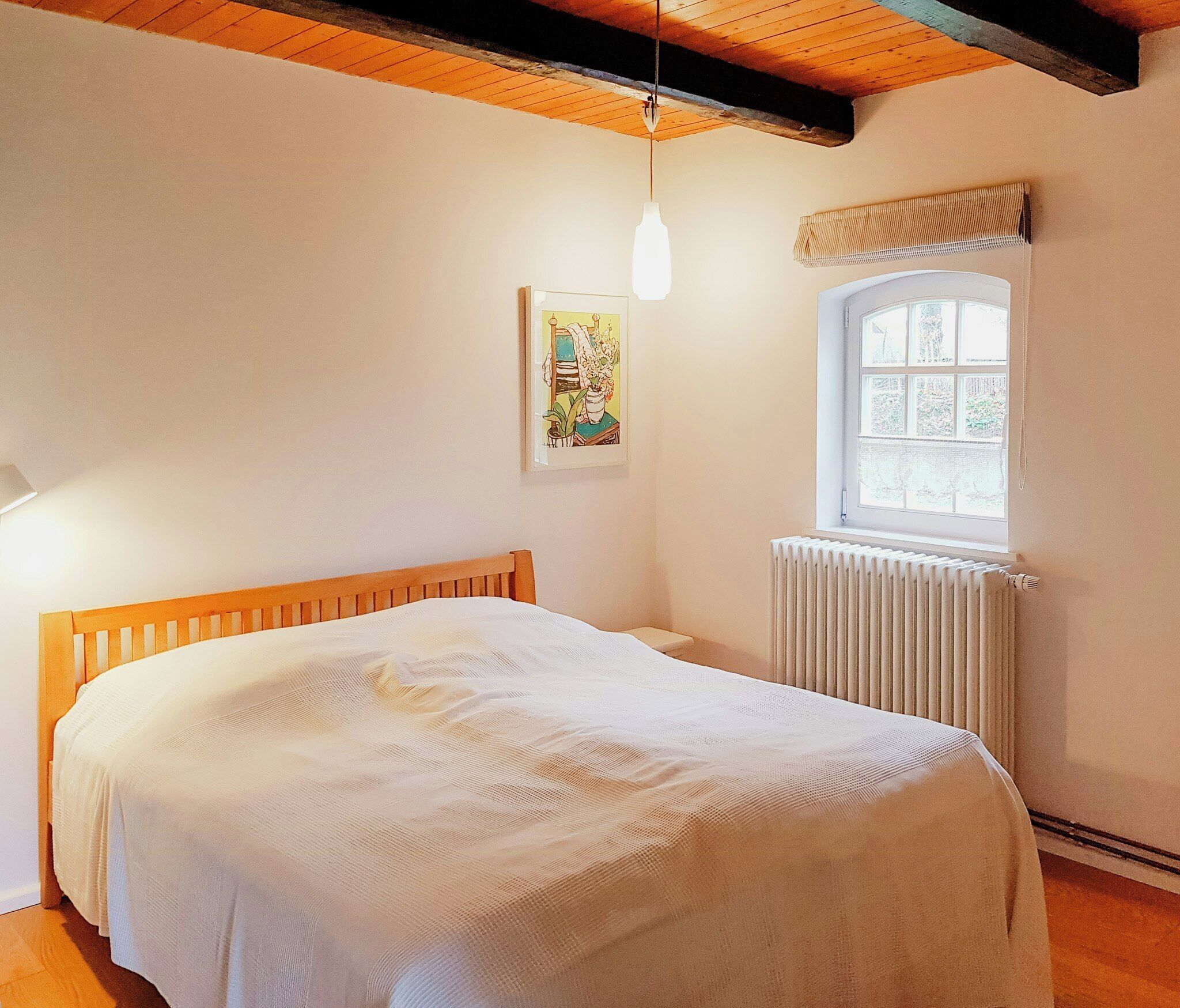 A bedroom with a wooden bed, a radiator, a window, and a hanging light fixture.